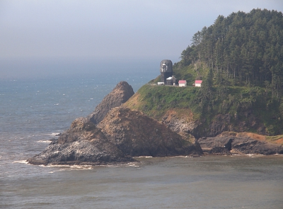 [A closer view of the left portion of the prior photo. The top of the lighthouse is shrouded with black netting completely covering the light. Several small outbuildings are visible to its right.]